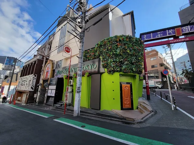 A bright green building with a plant wall and an orange door on a street corner