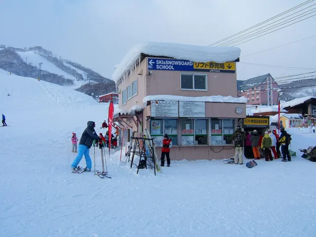 Skiers with poles and skis in front of a ticket building in the snow