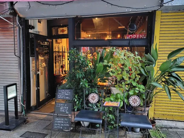 A narrow entrance with potted greenery, a red neon sign and chalkboards