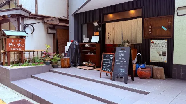 An entrance with wide steps, a cloth curtain, a chalkboard menu and potted plants on both sides