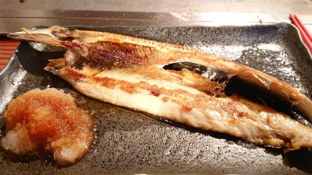 A whole grilled fish split open on a black plate, beside a mound of grated radish