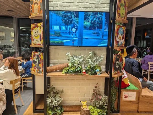 A cafe seating corner with illustrated panels, greenery and a small figurine on a log
