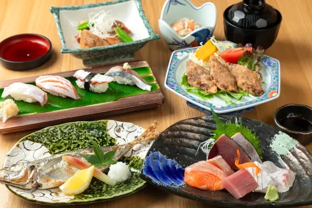 An assortment of dishes on a wooden table, including sushi, sashimi, grilled fish and fried pieces