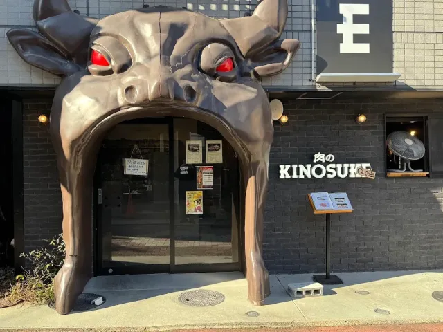 An entrance topped by a giant bull head sculpture with red eyes, beside a sign and a menu