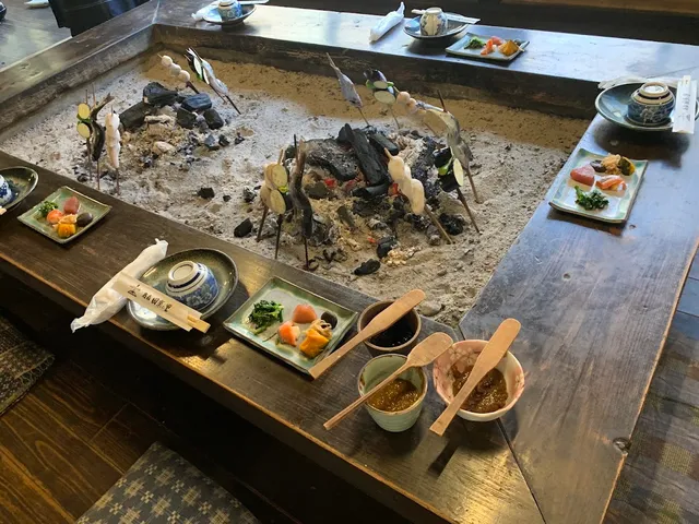 A sunken hearth with embers and skewers stuck in the ash, with small plates around it