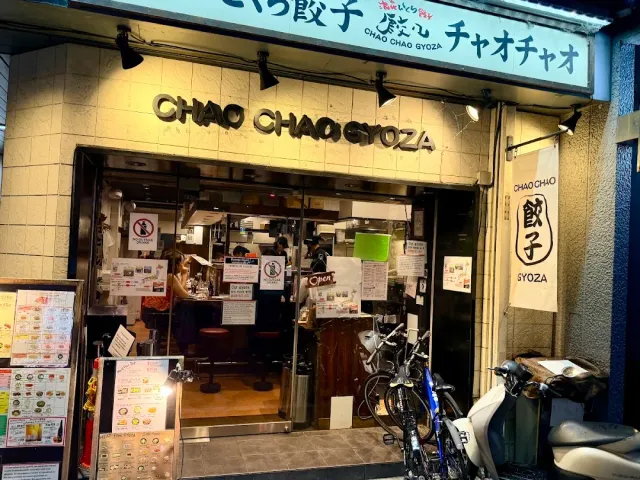 A frontage with gold lettering and a light blue sign, photo menus outside and parked scooters