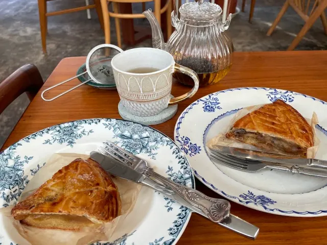 Two floral plates with a triangular brown pastry, a tea cup and a glass pot