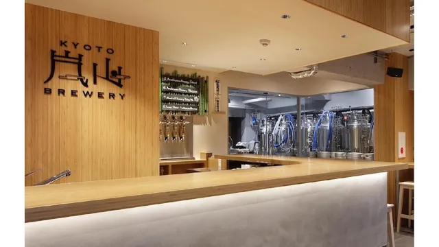 A pale wooden counter with beer taps, with stainless steel fermentation tanks behind it