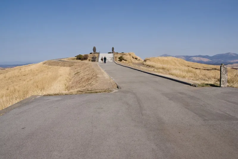 A path climbing a brown grass hill to a lookout, with visitors and a mountain ridge on the horizon