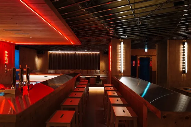 A wooden space with stools along long counters and red neon strips on the ceiling
