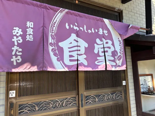 A purple fabric curtain with large white Japanese script, above sliding glass doors