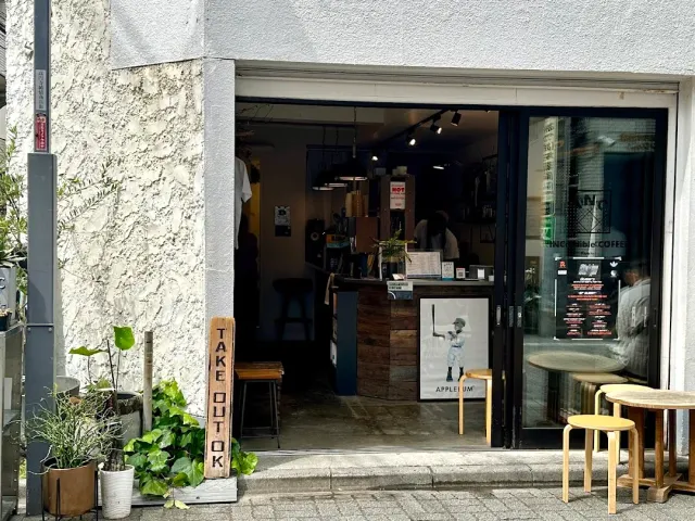 An open entrance with a vertical wooden sign, potted plants and wooden stools outside