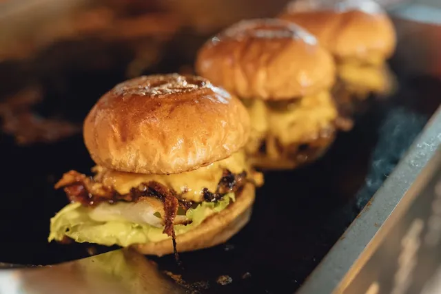 Three small burgers with melted cheese and caramelised onion on a hot griddle