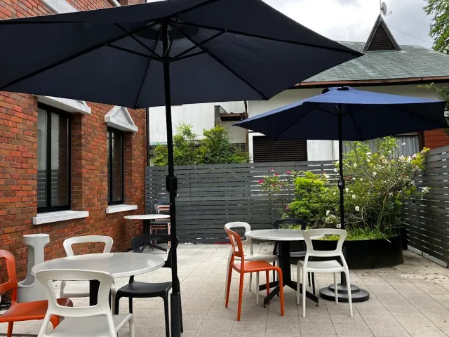 A paved patio with dark parasols, round tables and white and orange plastic chairs