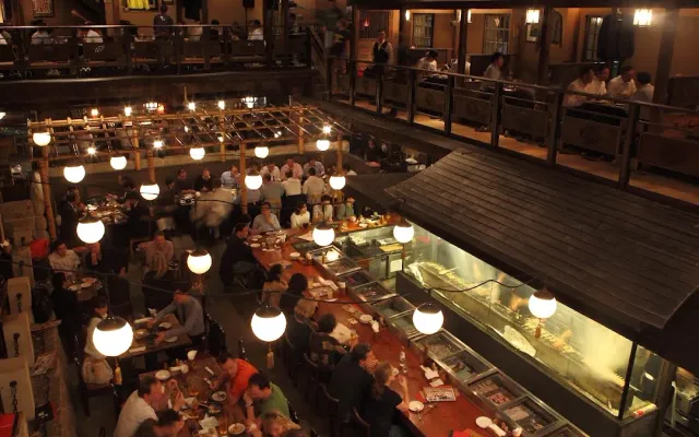 A crowded multi level wooden hall, with hanging paper lanterns and an open kitchen