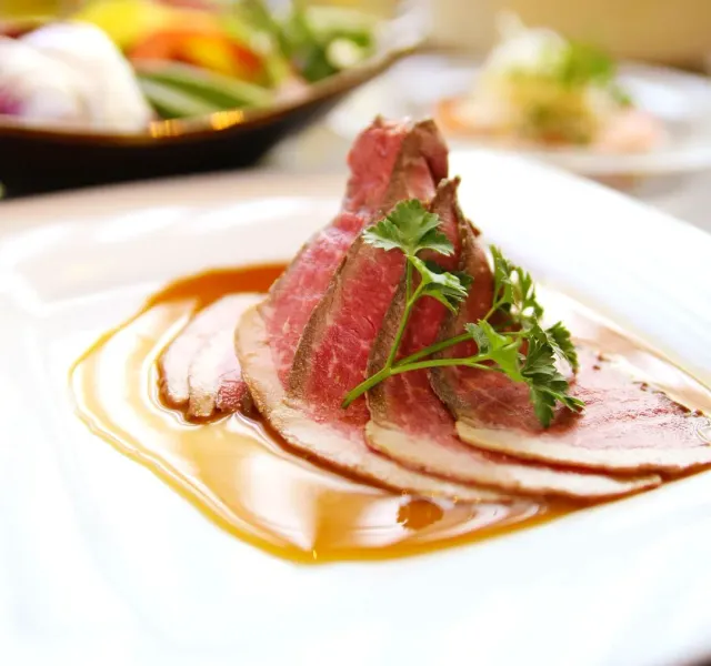 Pink meat slices on a white plate with brown sauce and herb leaves