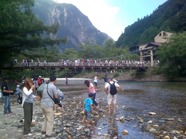 Walkers on the bank of a shallow river with a mountain ridge behind