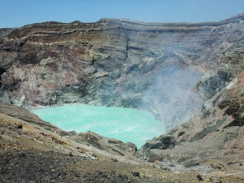 A volcanic crater with a turquoise lake and white steam rising from ash walls