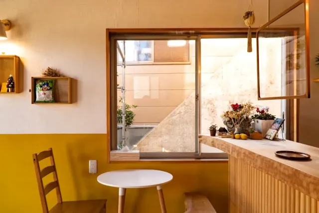 A small corner with a yellow wall, a round white table, a wooden chair and a window to the outside