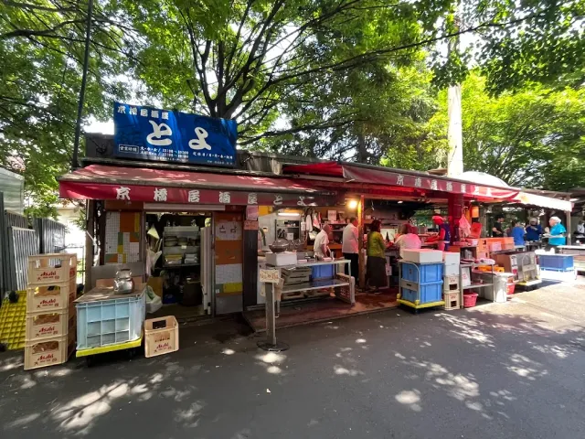 A street stall with a red awning, crates and workers preparing food under trees