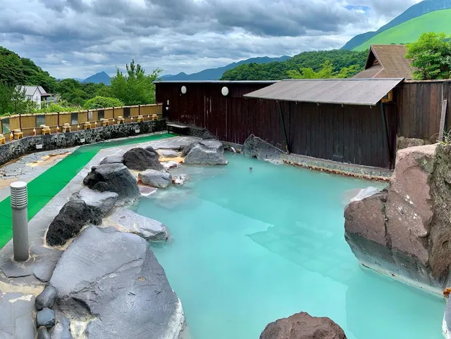 An outdoor pool of milky turquoise water among rocks, facing green mountains