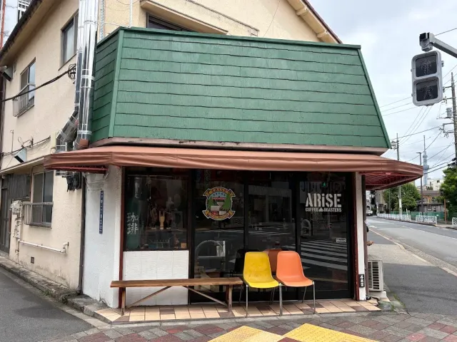 A corner building with a green shingled roof, a wide window and yellow and orange chairs