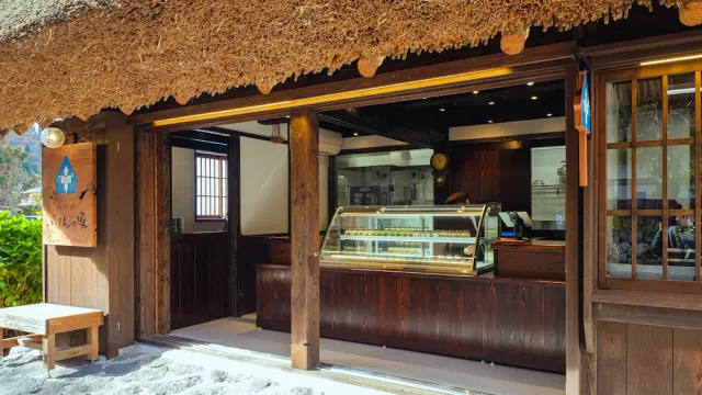 A front roofed with straw, and inside a display fridge with desserts and a dark wooden counter