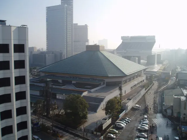 An arena with a square green roof among city buildings, seen from above