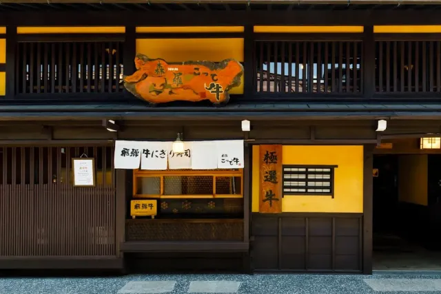 A traditional two storey wooden frontage with yellow walls, a carved sign and white banners