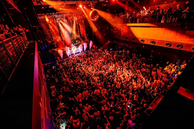 A dense crowd dancing in front of a stage with red lights and a mirror ball above the floor