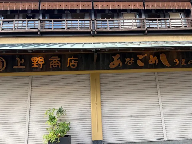 A shopfront with closed shutters and a carved wooden sign under a wooden balcony