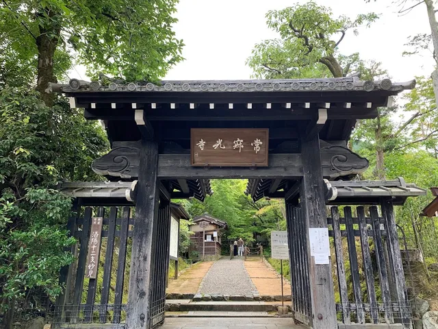 A dark wooden gate with an inscribed plaque, and beyond it a gravel path between green trees