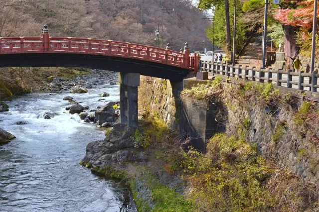 A red wooden bridge over a mountain river between rocks and trees