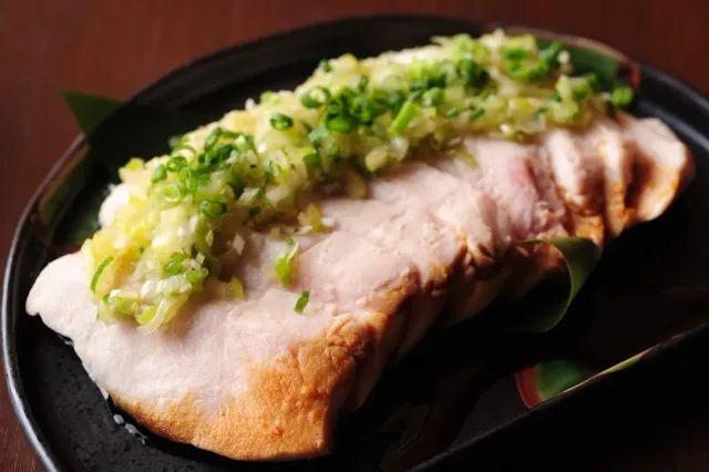 Slices of pale meat on a dark plate with chopped green onion on top