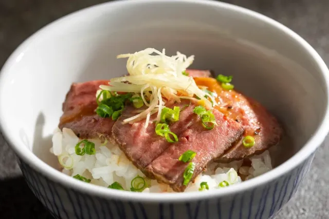 A white bowl with rice, pink slices of meat, spring onion and shredded ginger