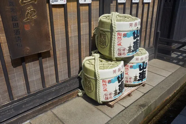 Straw-wrapped sake barrels stacked outside a dark wooden building