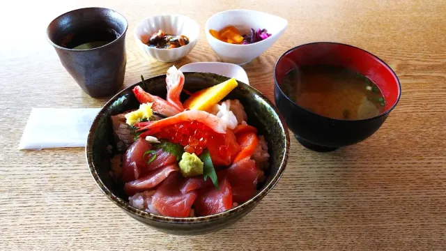 A rice bowl with slices of raw fish and orange fish roe, beside soup, tea and small side dishes