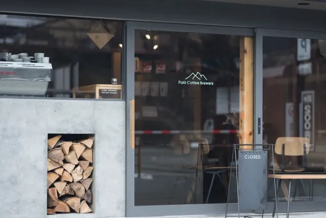 A shop window with a mountain sign, an espresso machine and a stack of logs in the concrete wall