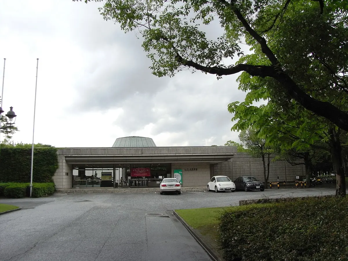 A pale museum building seen through trees, with a path leading in