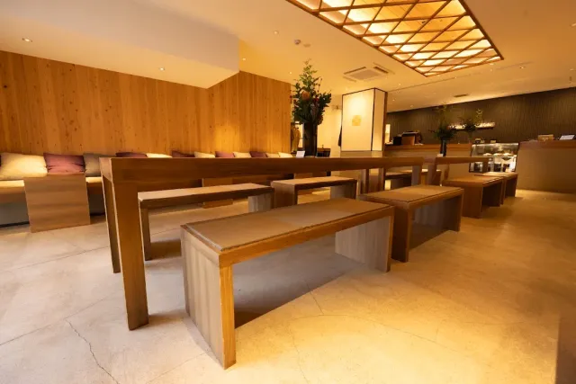 A wood clad hall with long benches, light upholstery and a lit lattice ceiling