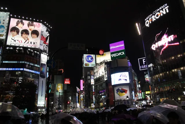 A city crossing at night with giant advertising screens and crowds of pedestrians
