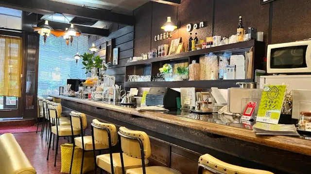 A long wooden counter with yellow bar chairs and old style hanging lamps