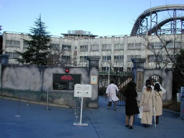 A grey attraction building with roller coaster track above it and visitors at the entrance
