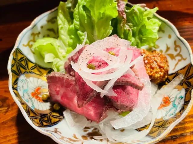 A painted bowl with slices of pink meat, onion rings, lettuce leaves and a spot of grainy sauce