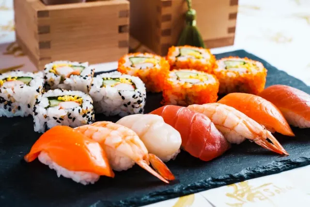 A slate tray with fish nigiri and rolls coated in sesame and orange fish roe
