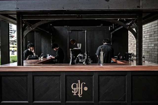 A wide dark wooden counter with three workers preparing coffee behind it