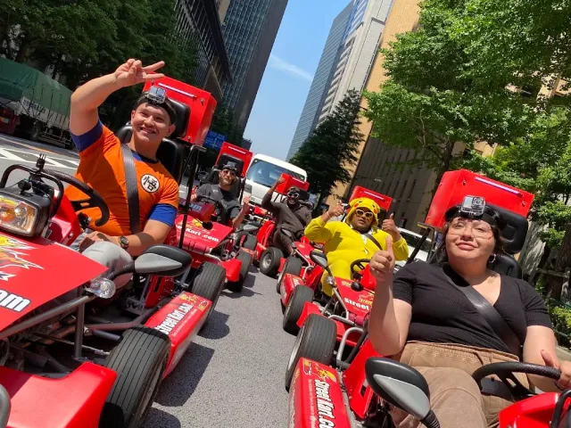 Five riders in red go karts on a city street, gesturing toward the camera