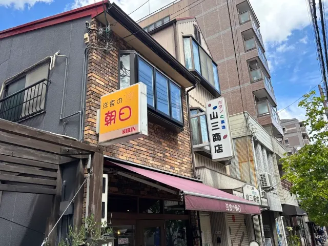 A brick building on a street with a lit orange sign, a pink awning and neighbouring shop signs