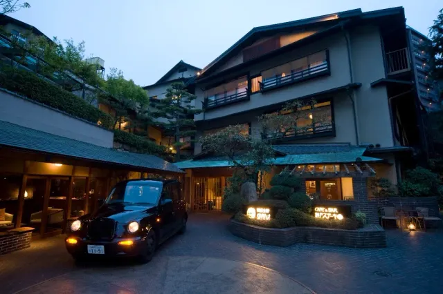 A multi storey wooden inn building at dusk, with a black taxi parked in front