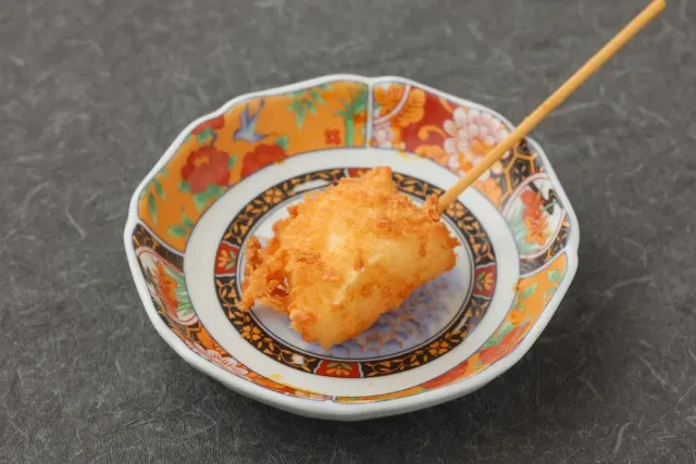 A fried battered piece on an orange patterned plate, with a wooden skewer